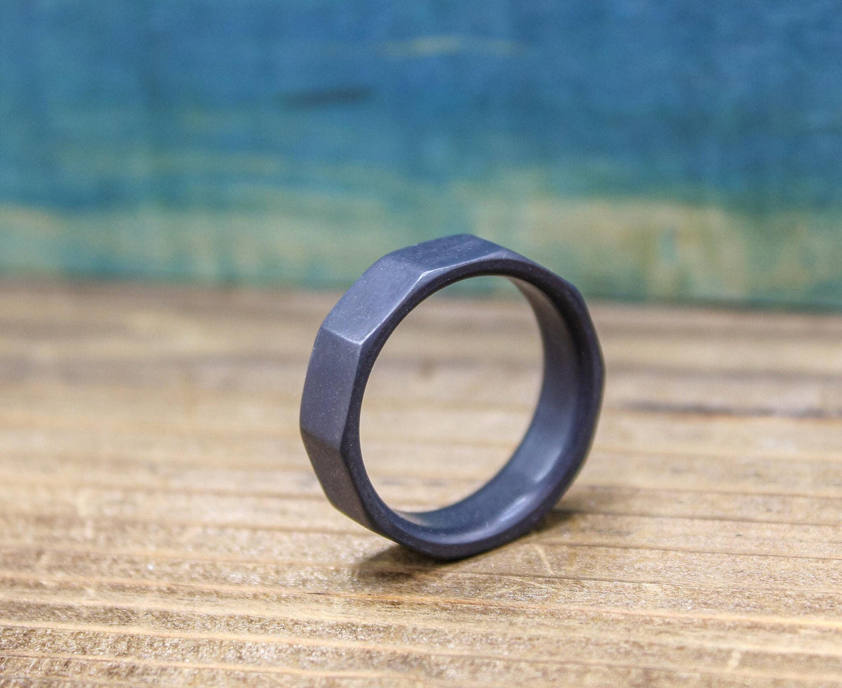 A dark gray, ten-sided ring stands on its edge on a light brown wooden surface, with a blurred blue background.
