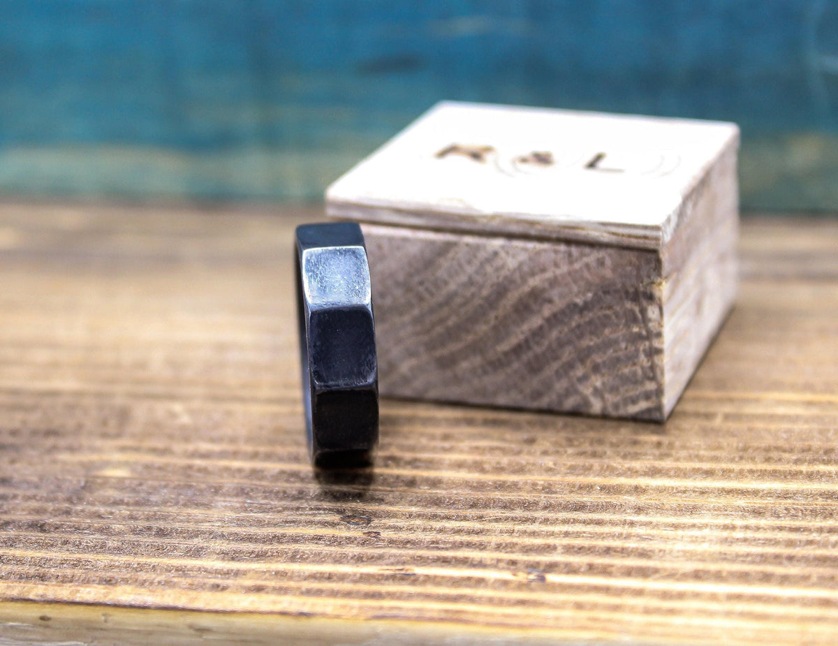 A dark gray, ten-sided ring stands on its side in the foreground, with a closed light wooden box in the blurred background.