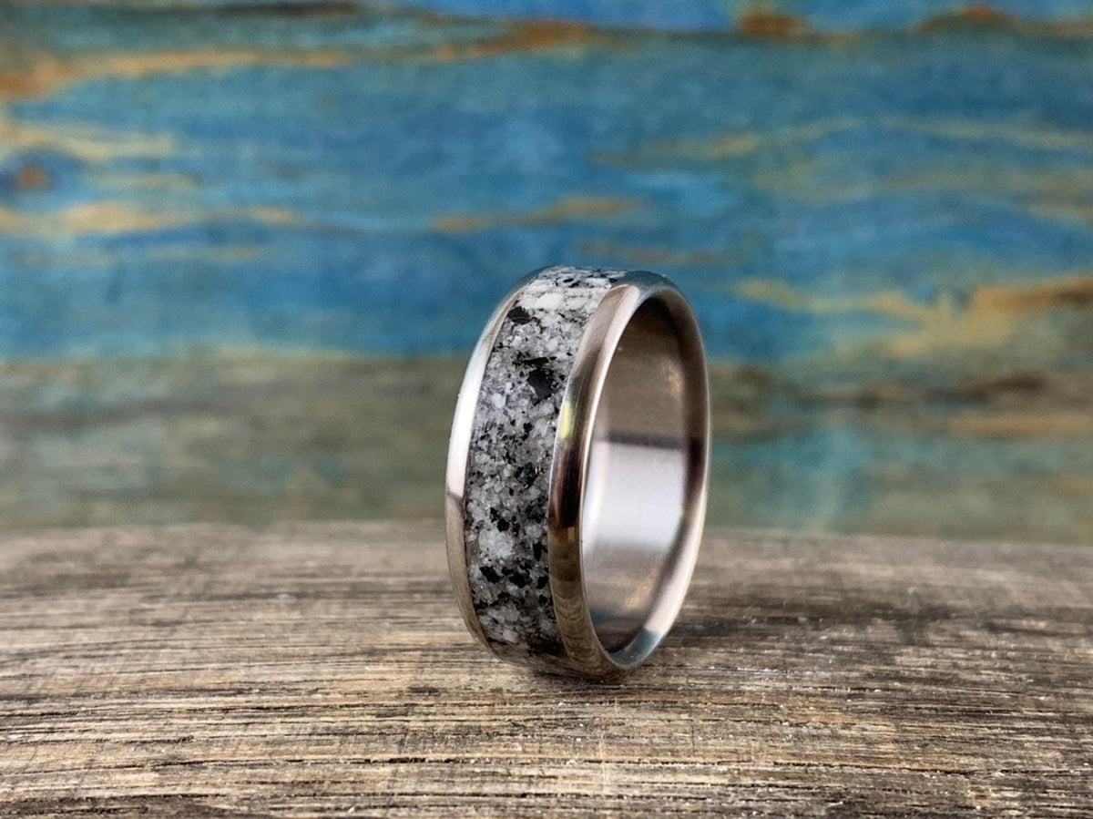 A silver-colored ring with a speckled gray and white granite inlay stands upright on a light brown wooden surface.