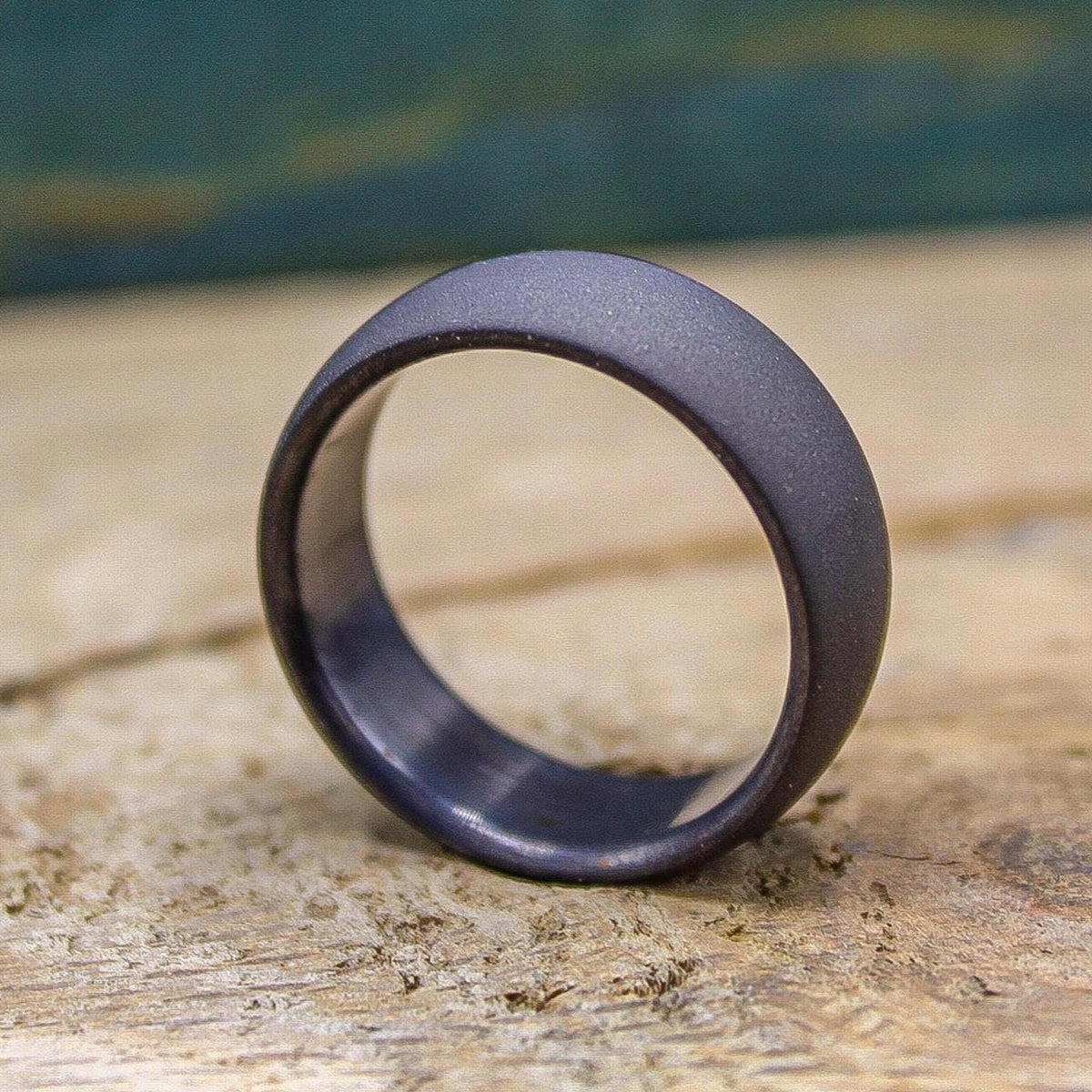 A dark gray, sandblasted ring with a smooth interior, resting on a light wooden surface.