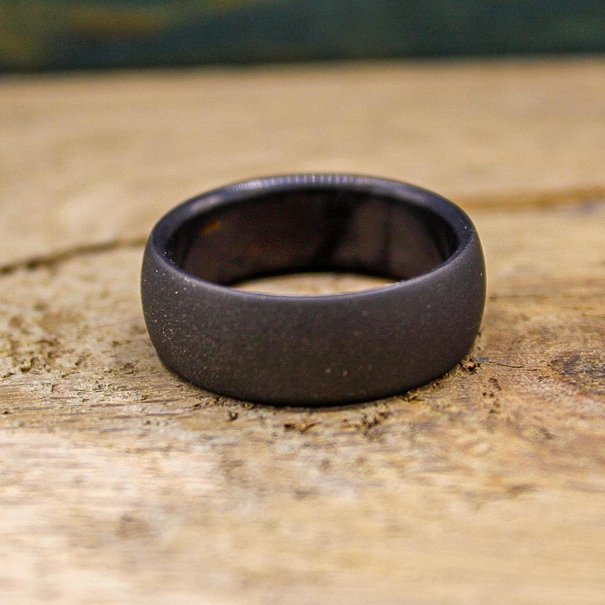 A dark gray, sandblasted ring with a smooth interior, viewed from the top on a light wooden surface.