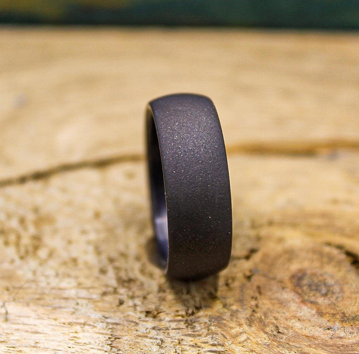A dark gray, sandblasted ring with a smooth interior, viewed from the side on a light wooden surface.