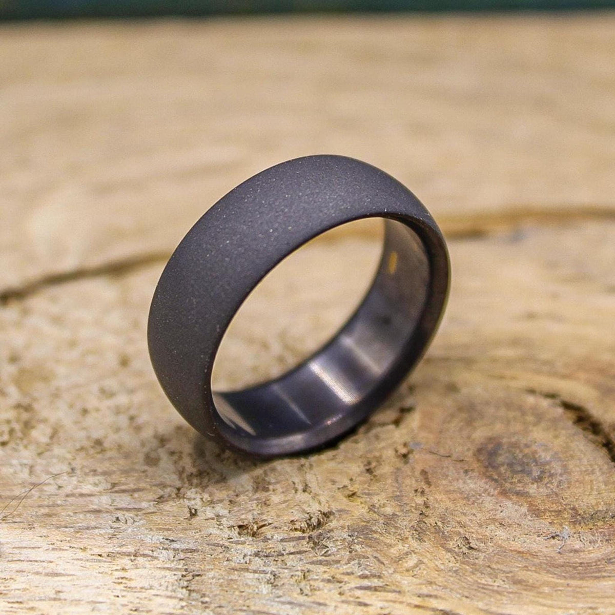 A dark gray, sandblasted ring with a smooth interior, angled on a light wooden surface.