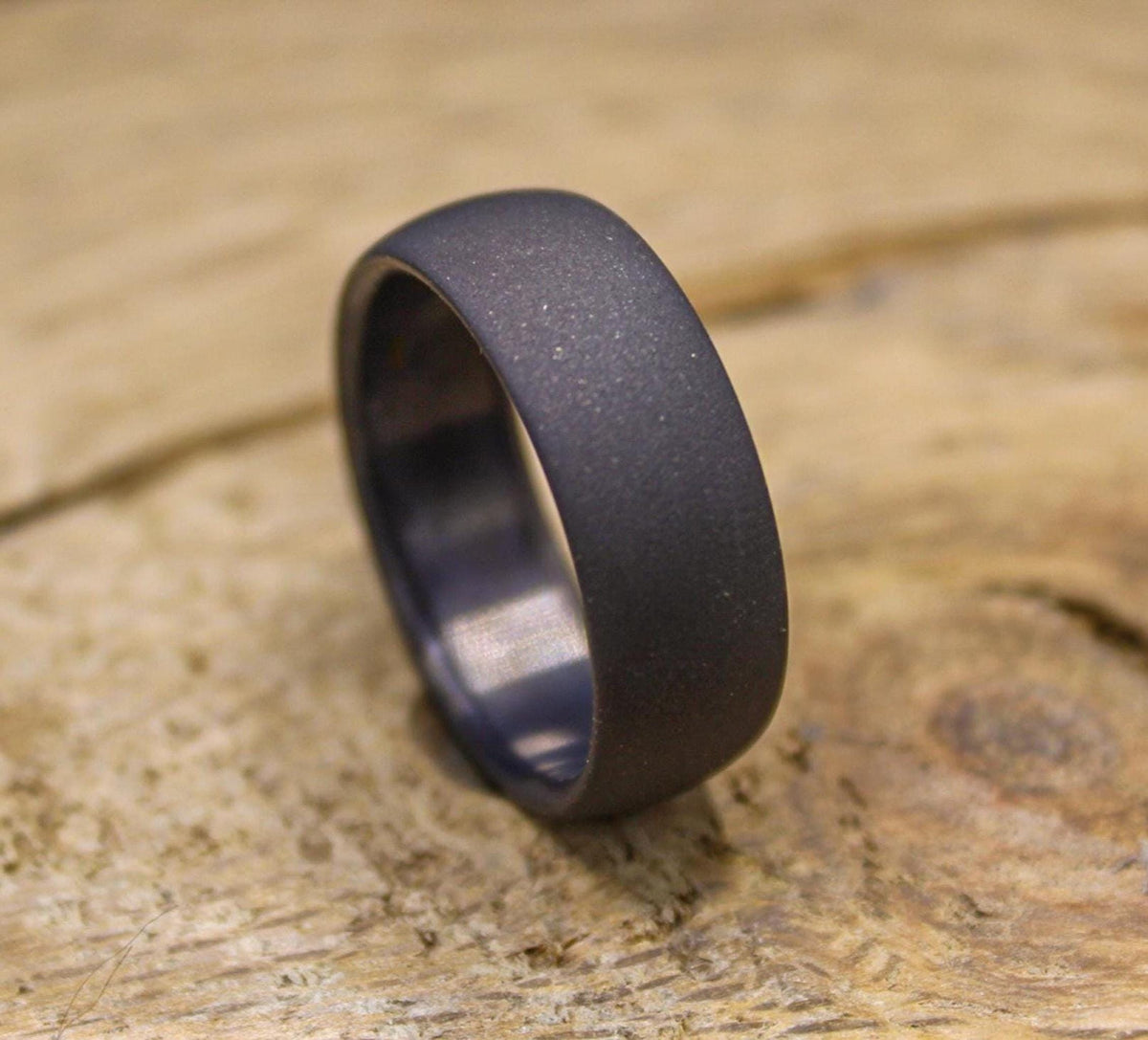 A dark gray, sandblasted ring with a smooth interior, angled on a light wooden surface.
