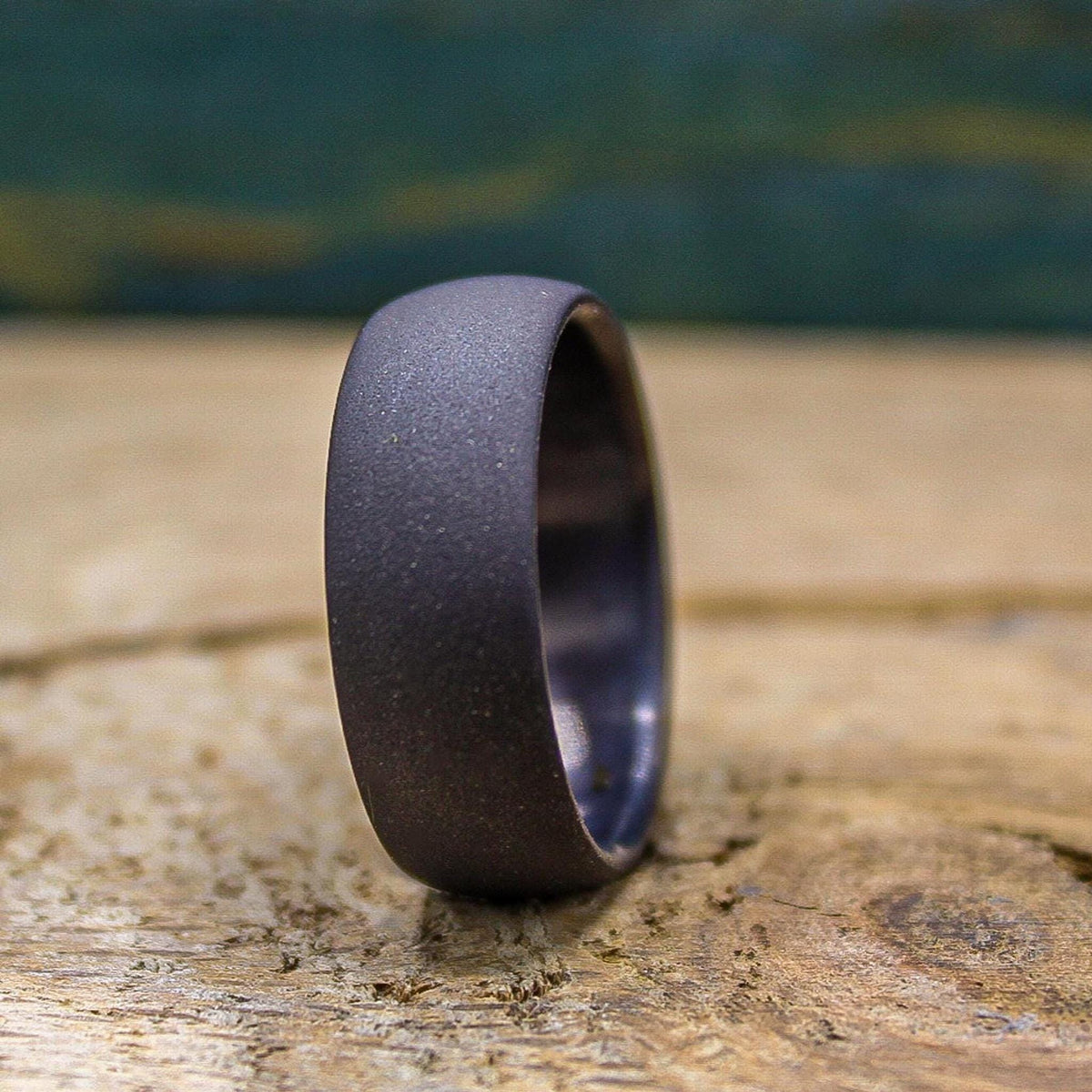 A dark gray, sandblasted ring with a smooth interior, angled on a light wooden surface.