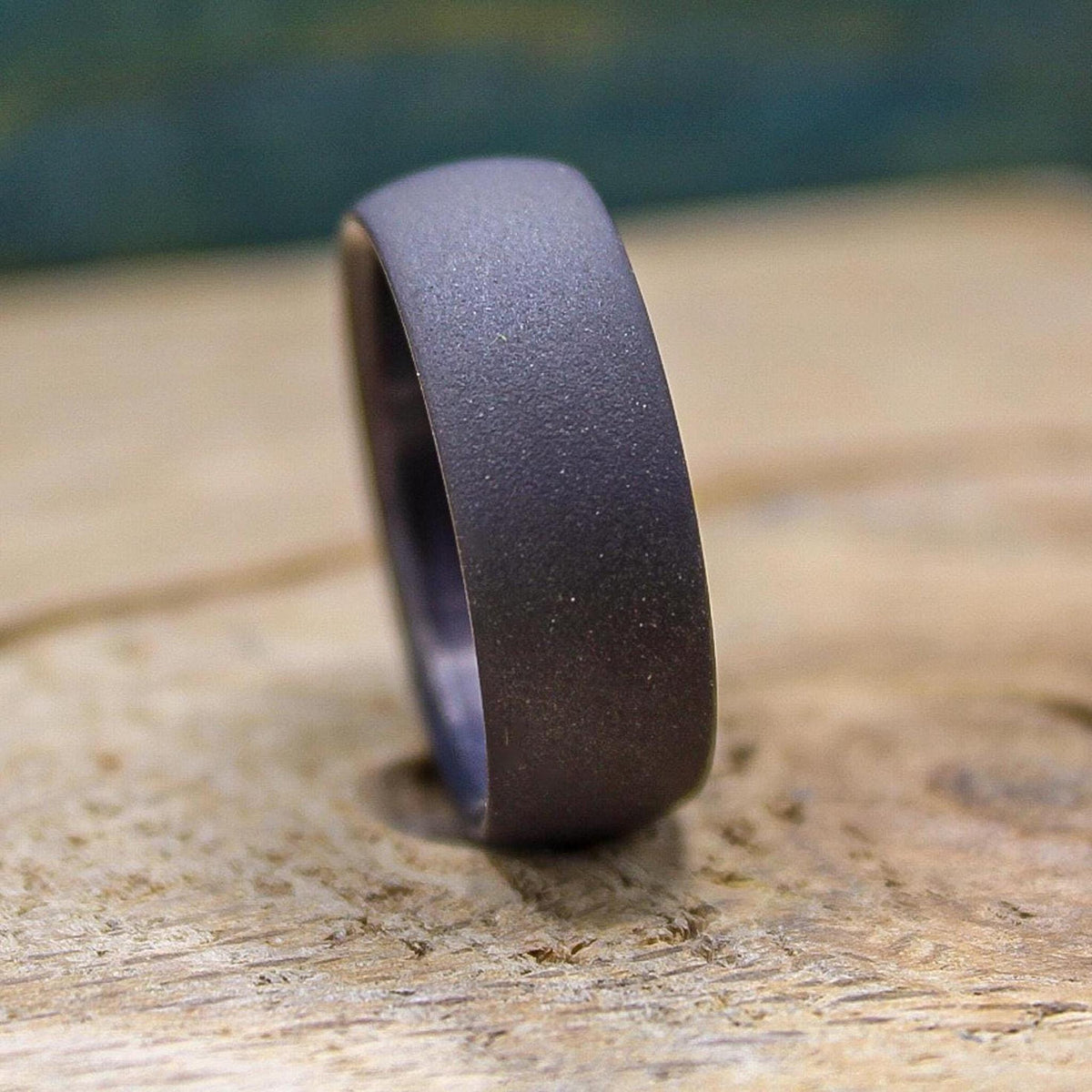 A dark gray, sandblasted ring with a smooth interior, viewed from the side on a light wooden surface.