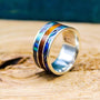 A sterling silver ring resting upright on a wooden surface, featuring inlaid bands of iridescent blue abalone shell and brown mahogany wood.
