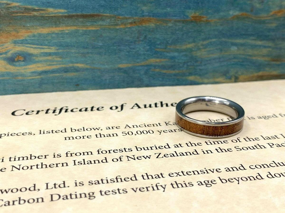 A silver-colored ring with a brown wood inlay rests on a partially visible "Certificate of Authenticity" document.