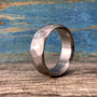 A silver-colored hammered titanium ring resting vertically on a wooden surface against a blue and brown background.