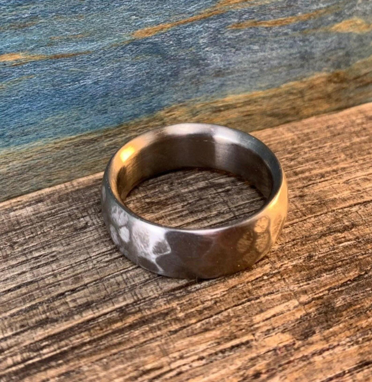 A silver-colored hammered titanium ring resting flat on a wooden surface in warm lighting.