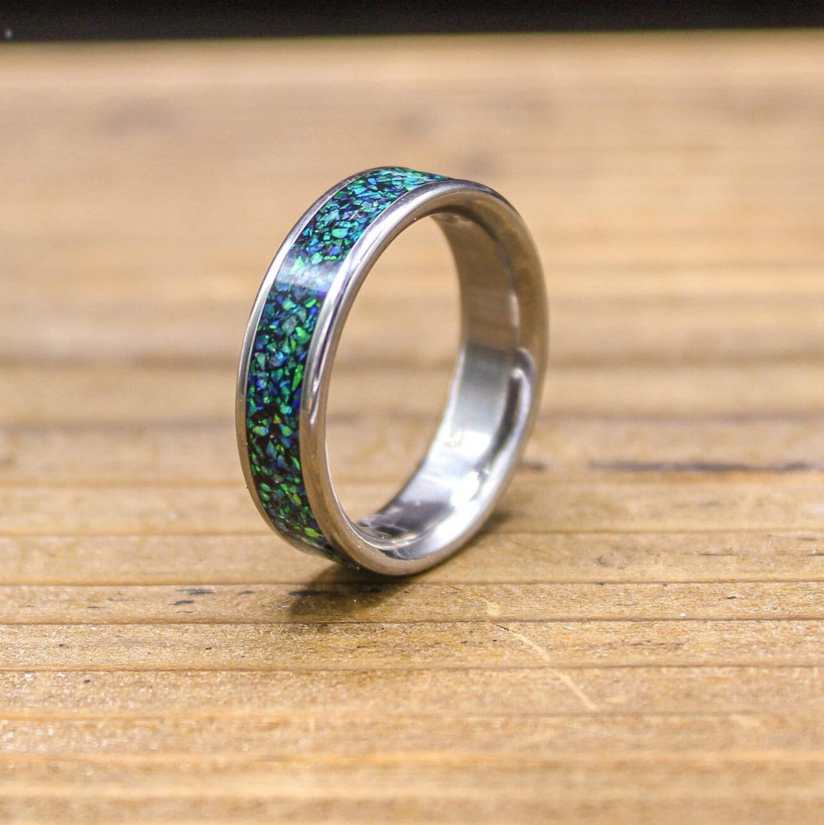 A silver-colored ring with a green and blue speckled inlay is slightly angled on a wooden surface.