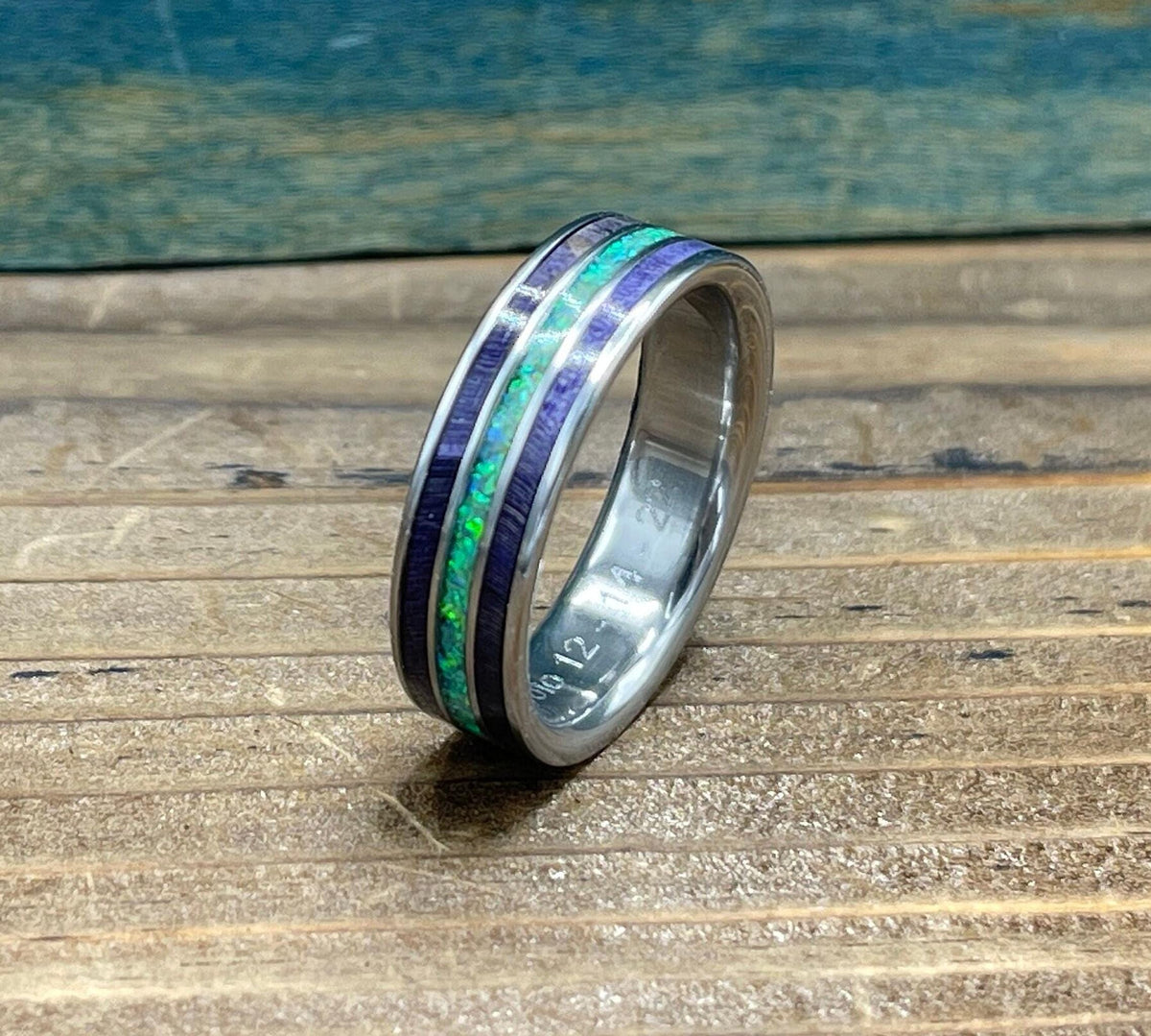 A silver ring with purple wood and green opal inlay is shown at an angle, with "OLO 12 1-4 2" engraved on the inside band.