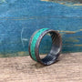 A Damascus steel ring with a malachite inlay, angled on a wooden surface with a blue background.