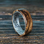 A zebrawood ring with a silver interior featuring an engraved floral pattern is angled on a dark wooden surface.