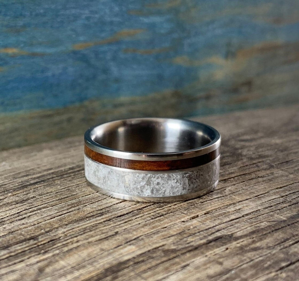 A titanium ring with a wide band of white rose quartz and a narrow strip of dark kingwood, shown from the side on a wooden surface.