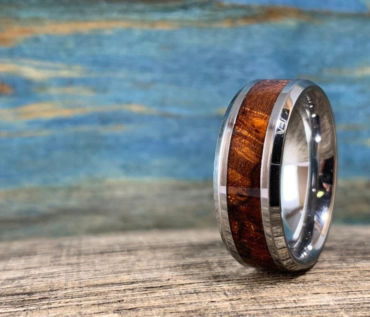 A silver-toned ring with a central ironwood inlay, angled to the right on a wooden surface with a blue and brown background.
