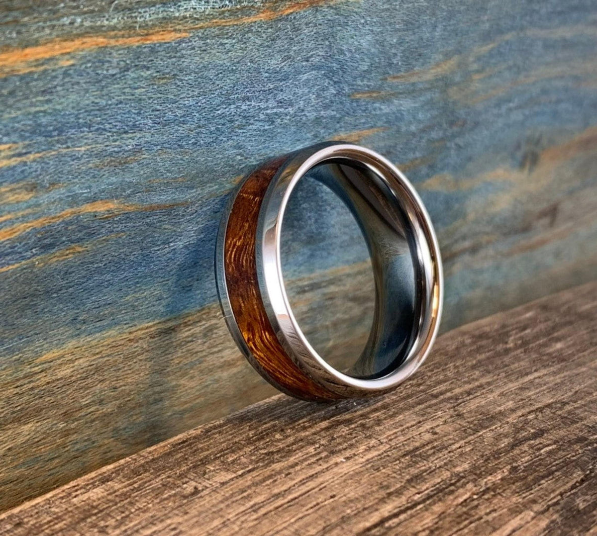 A silver-toned ring with a central ironwood inlay, with the inside of the band visible, on a wooden surface with a blue and brown background.