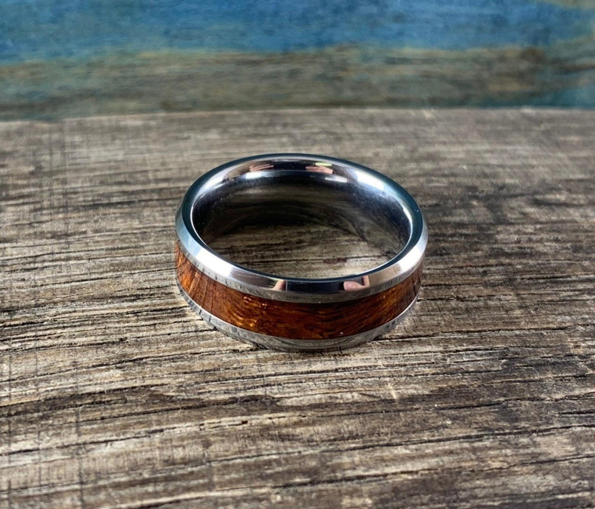 A silver-toned ring with a central ironwood inlay, viewed from the top on a wooden surface with a blue and brown background.