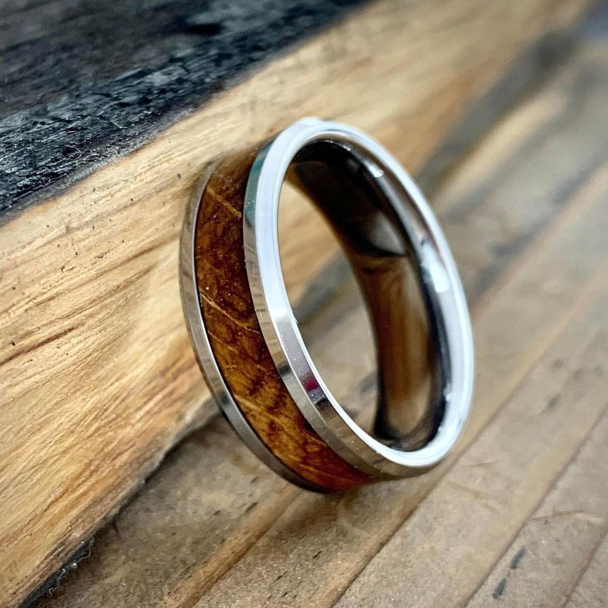 A silver-colored ring with a central band of light brown wood, angled on a wooden surface.