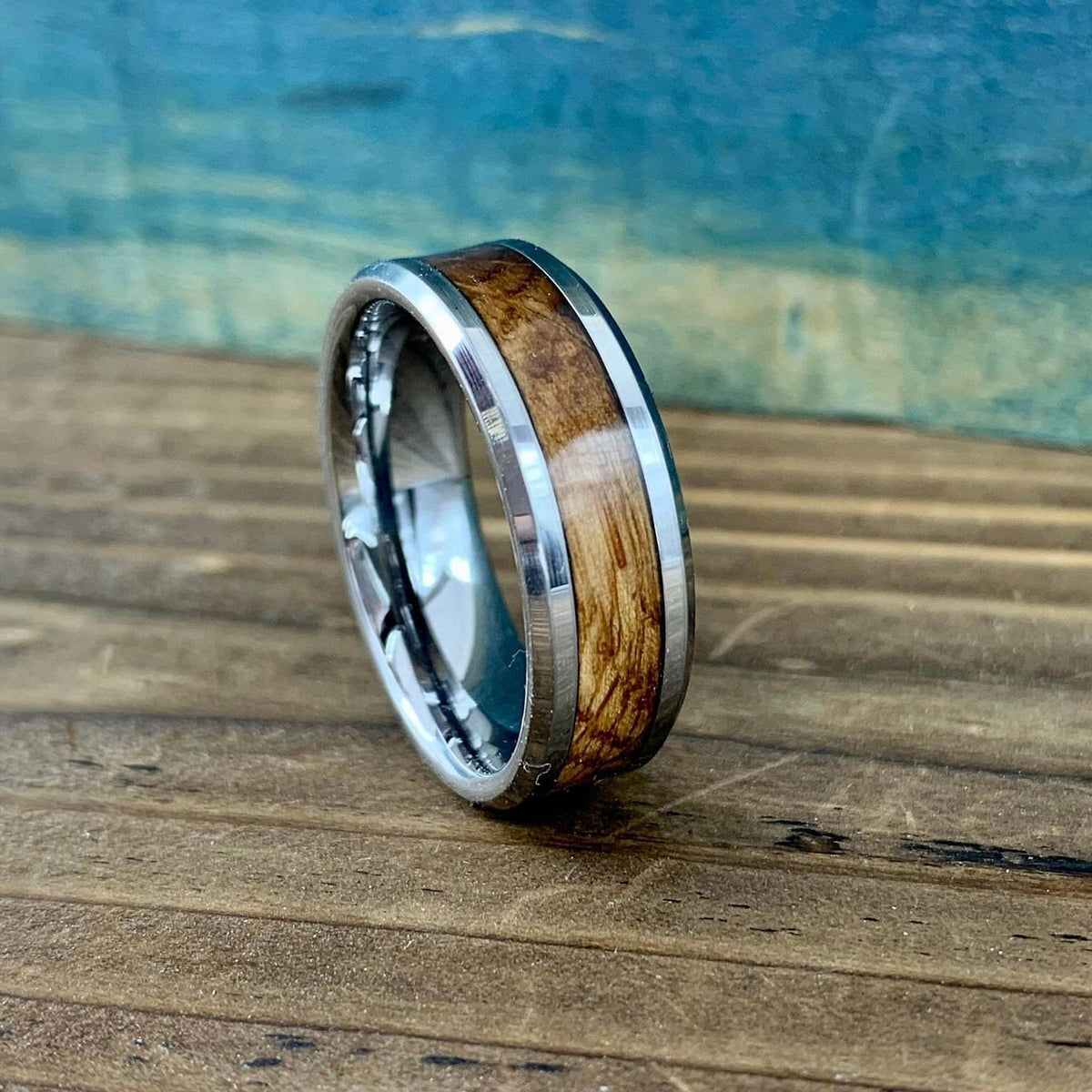 A silver-colored ring with a light brown wood inlay, on a wooden surface with a blue background.
