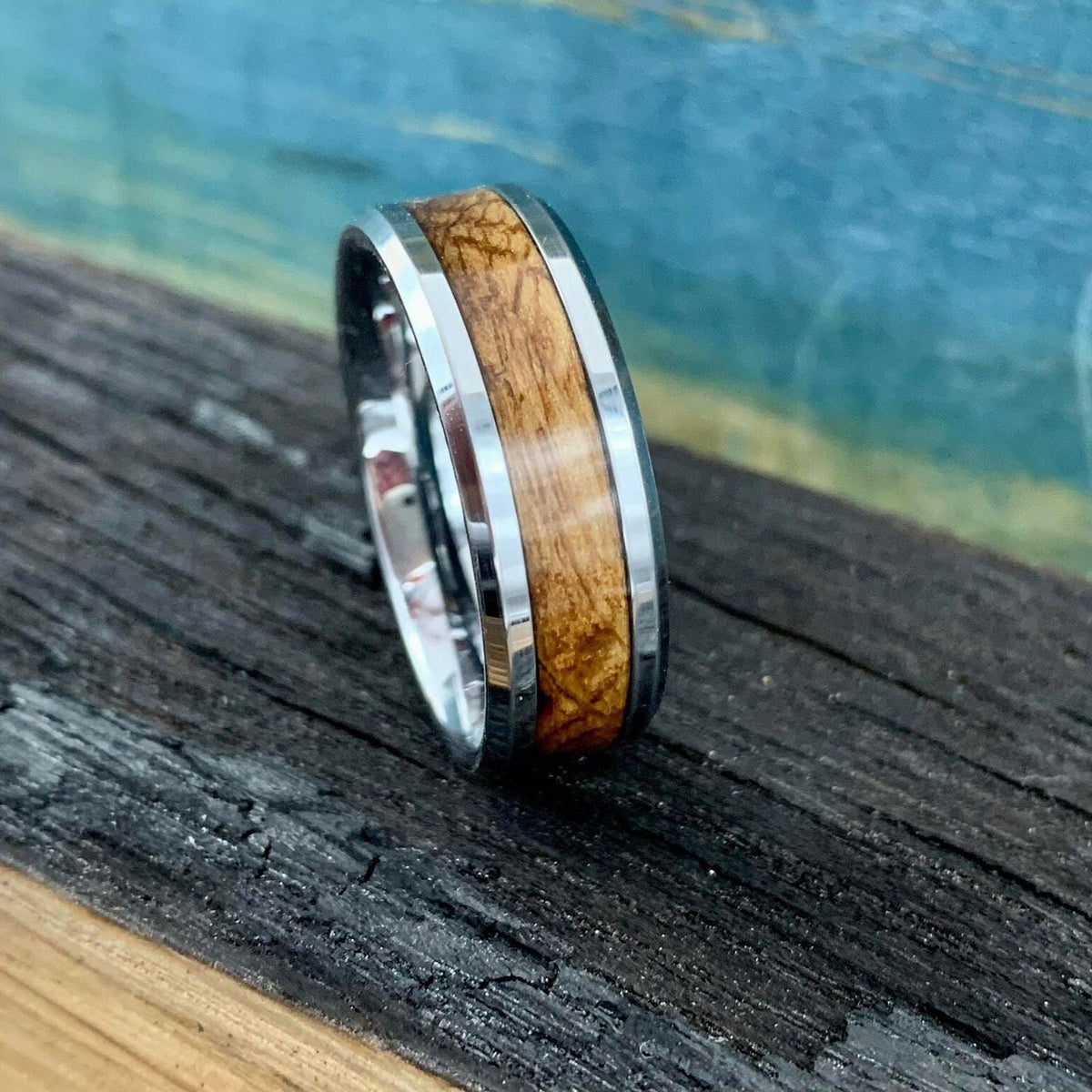 A silver-colored ring with a light brown wood inlay, on a dark wooden surface with a blue background.