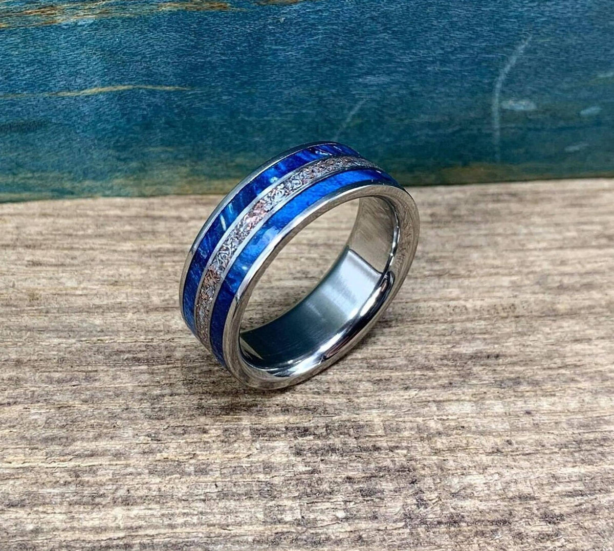 The ring stands upright on a textured wood surface, highlighting its polished interior and inlay design.
