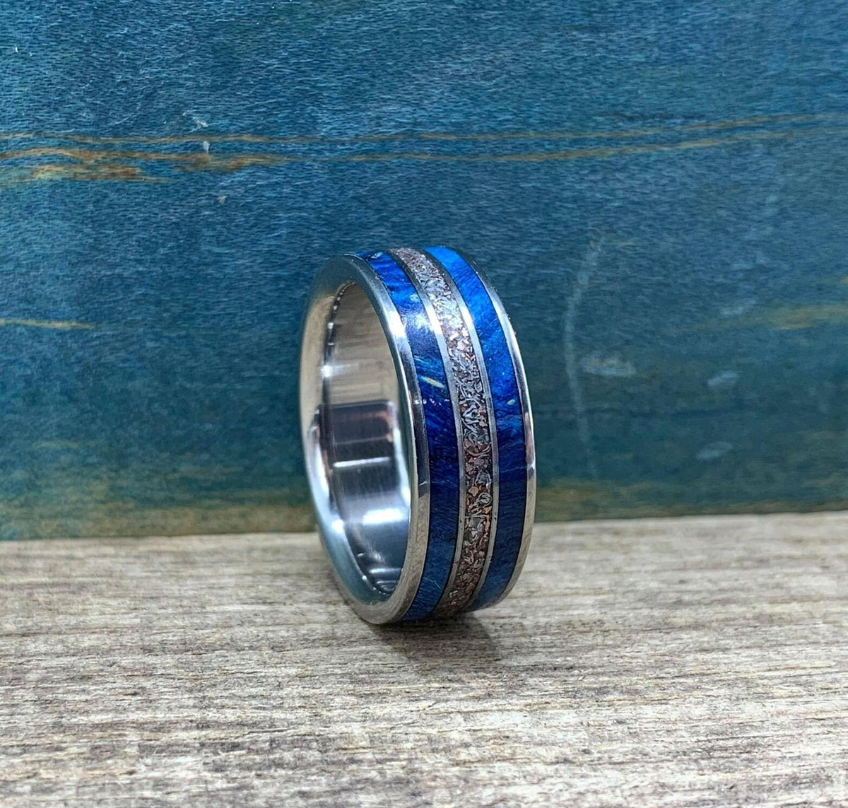 A side angle view of the ring sitting on a wooden surface, showing the detailed blue and metallic inlay.