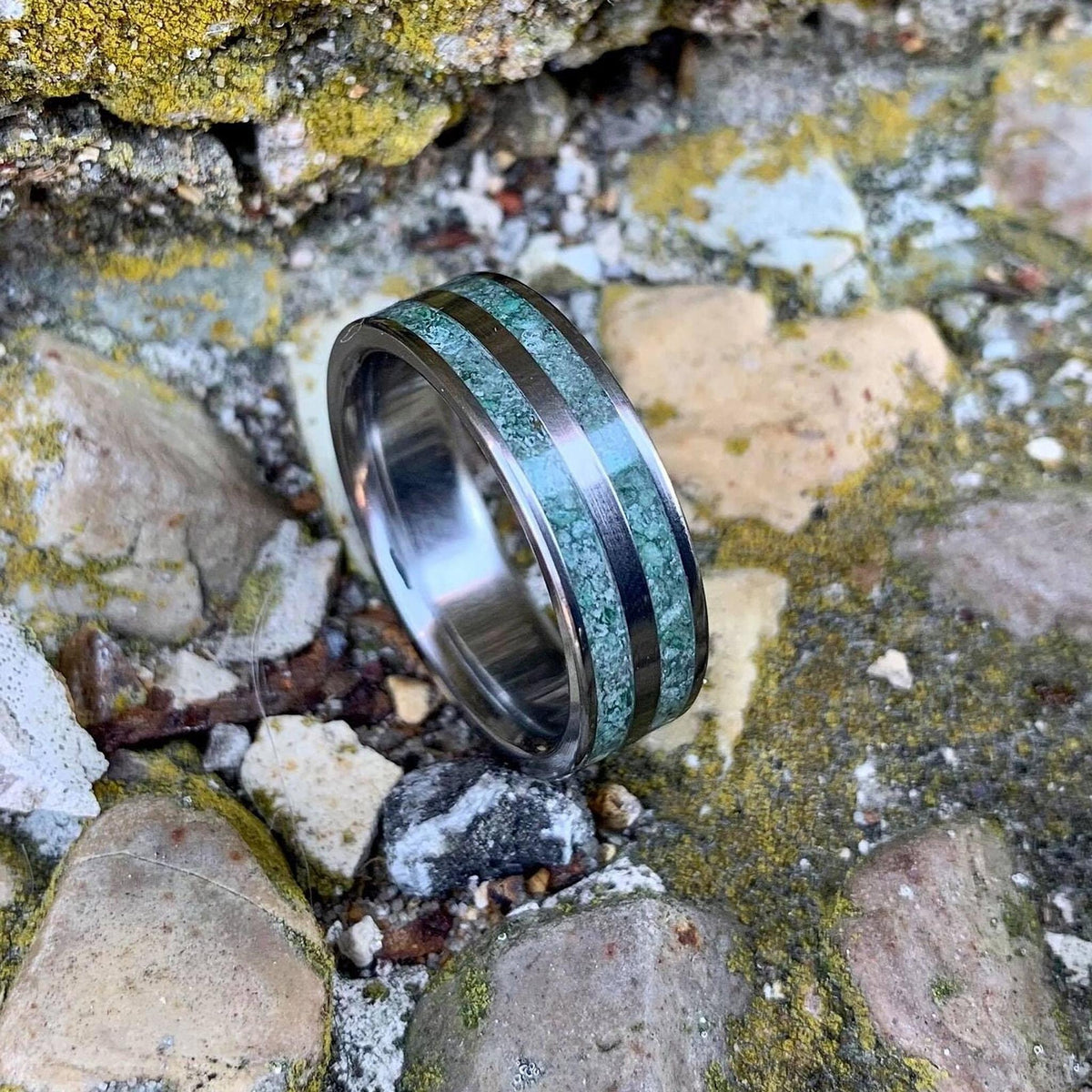 A close-up shot focuses on the dual green moss agate bands inlaid into the center of a polished titanium ring.