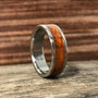 A metal ring with a warm wood inlay stands upright on a rustic wooden surface.