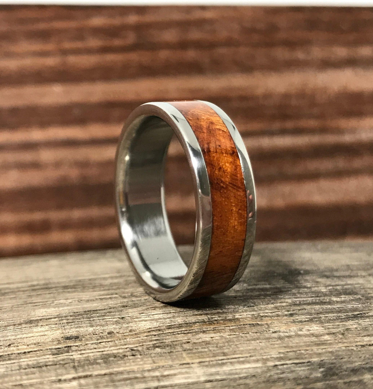 A metal ring with a warm wood inlay stands upright on a rustic wooden surface.