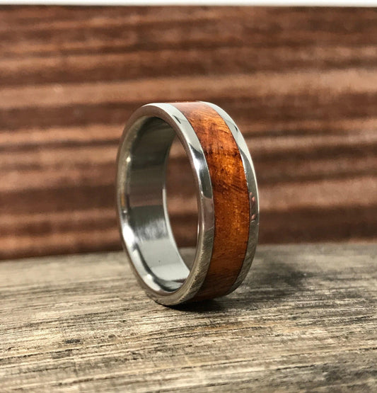 A metal ring with a warm wood inlay stands upright on a rustic wooden surface.