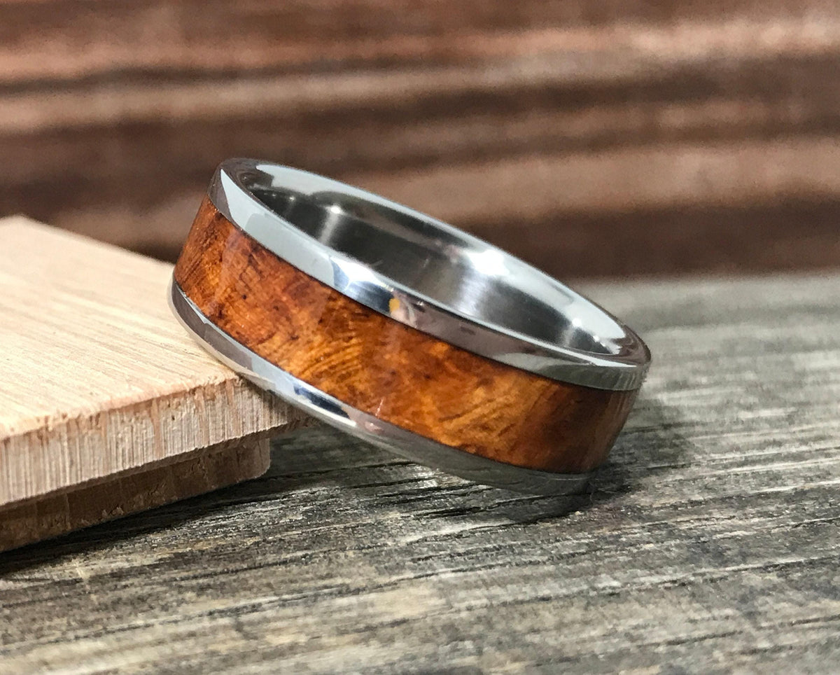 A metal and wood ring leans against a piece of wood on a textured surface.