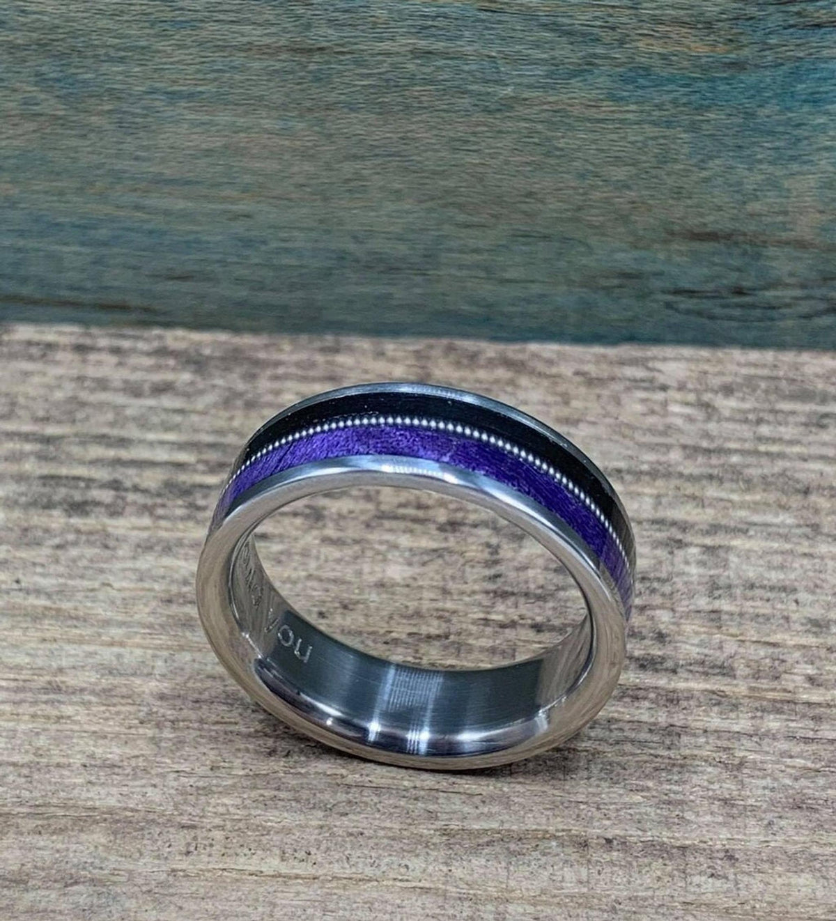 The ring resting on its side on a textured surface, displaying the continuous circular pattern of the ebony and purple wood.