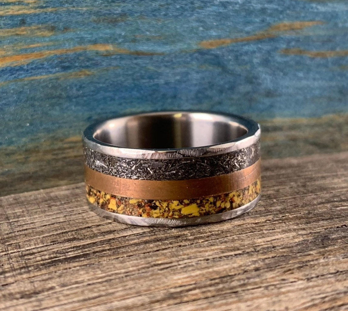 A silver-colored ring with smooth outer edges, a textured copper-colored band, and a textured yellow-orange band in the center.