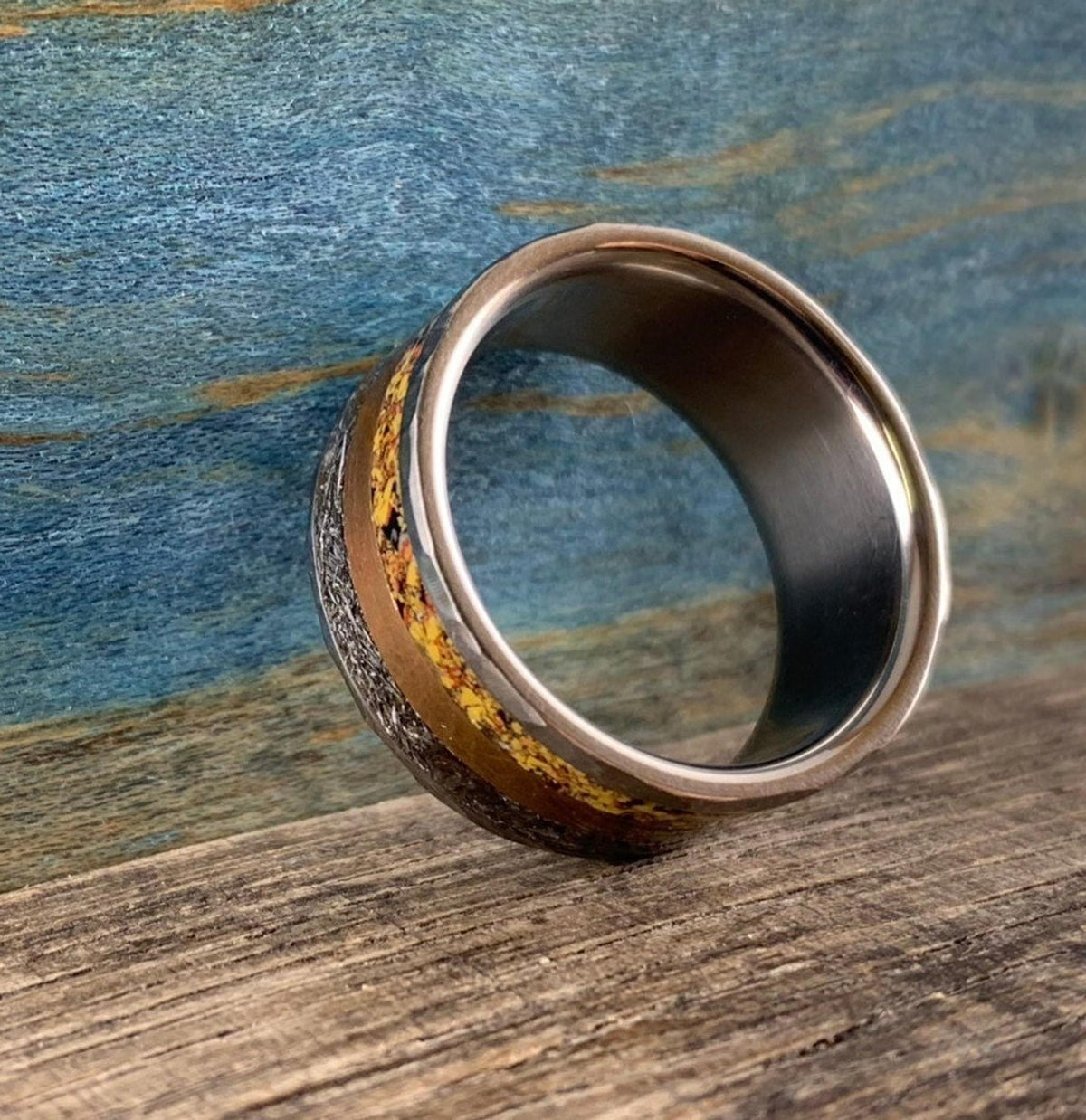 A silver-colored ring with smooth outer edges, a textured copper-colored band, and a textured yellow-orange band in the center, viewed from a low angle.