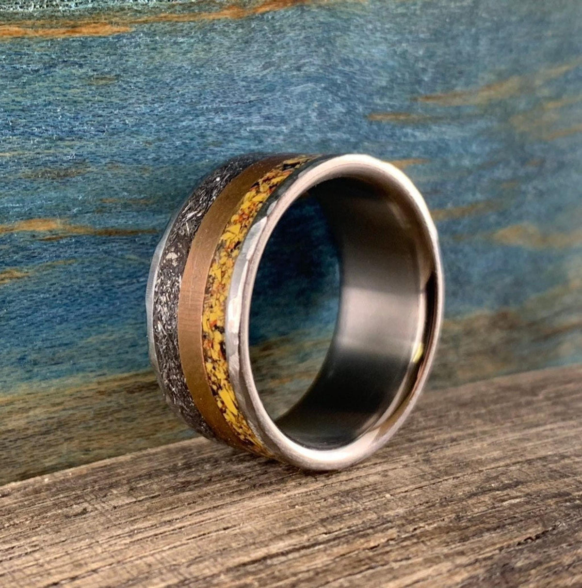 A silver-colored ring with smooth outer edges, a textured copper-colored band, and a textured yellow-orange band in the center, viewed from a slightly higher angle.