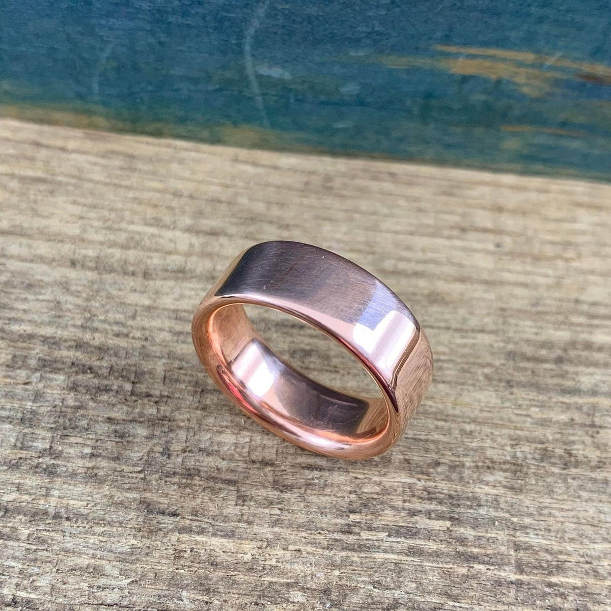 A matte rose gold-colored ring with a slightly rounded top surface is angled on a wooden surface.