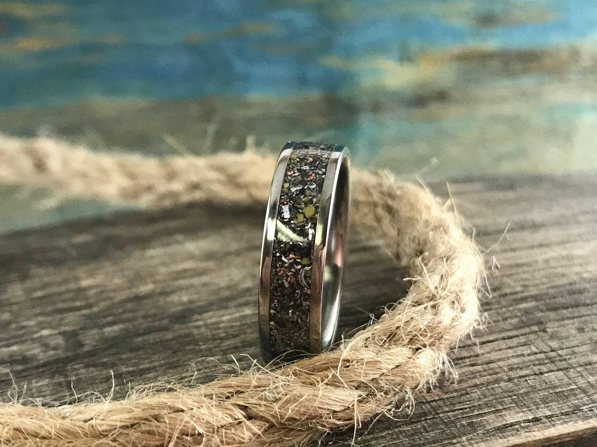 A silver-colored ring with a speckled, multi-colored inlay is positioned on a thick, coiled rope on a wooden surface.