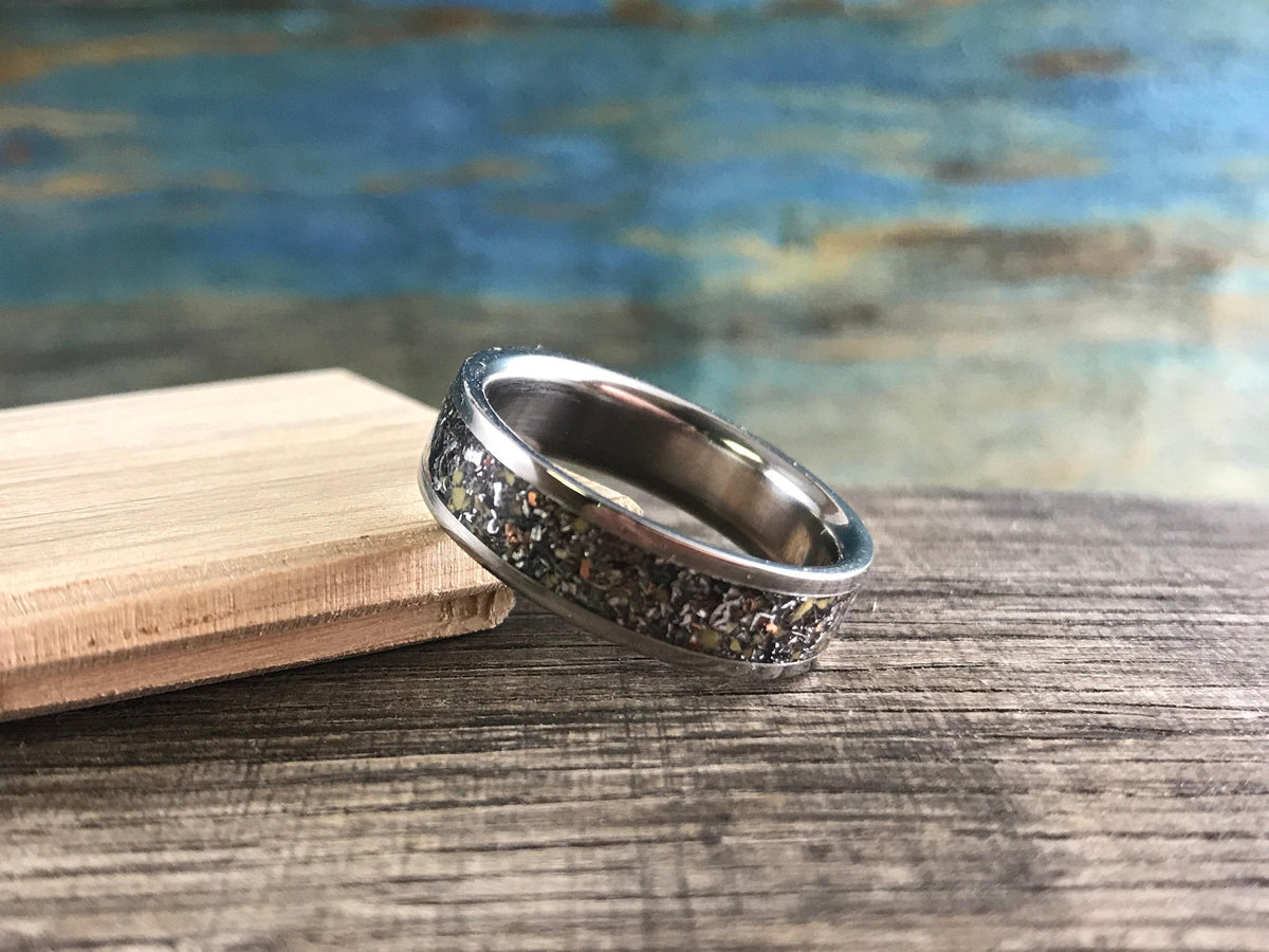 A silver-colored ring with a speckled, multi-colored inlay is angled on a light wooden block on a weathered wooden surface.