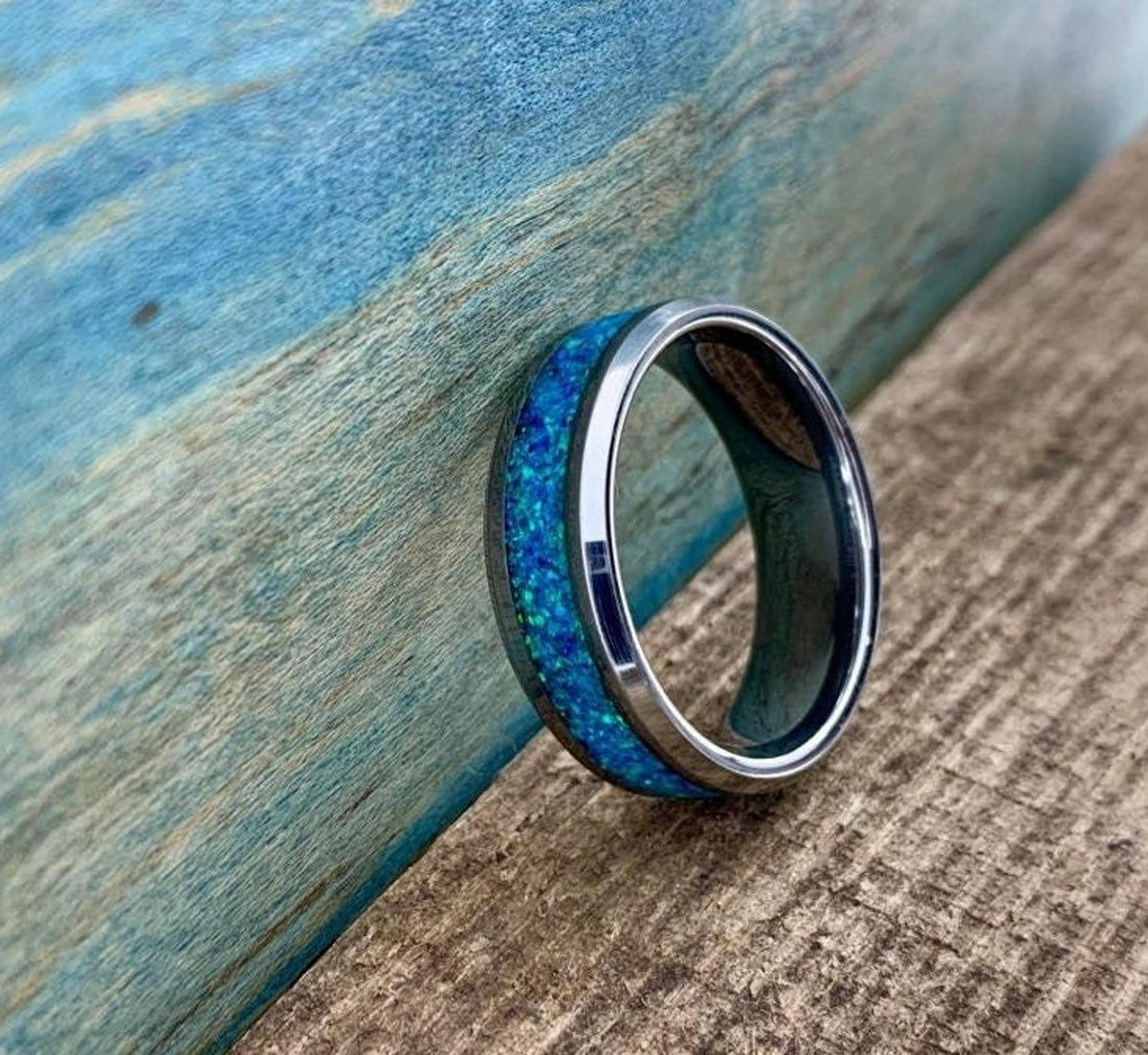 A silver-colored ring with a blue-green opal inlay is shown from a side view, revealing the inner band.