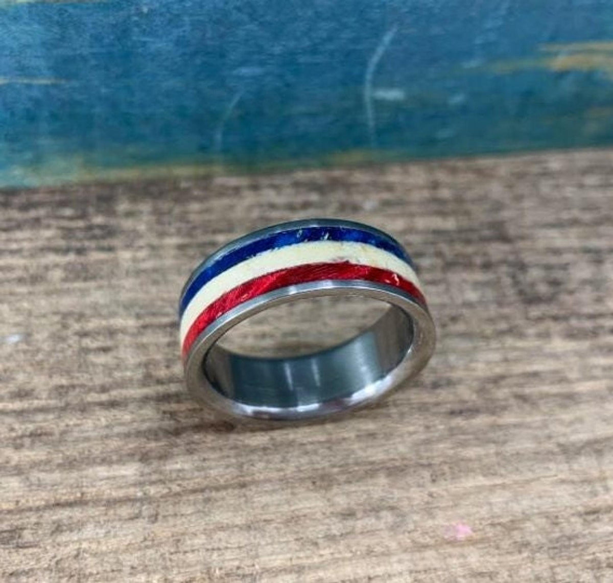 A silver-colored ring with red, white, and blue stripes is shown from a low angle on a wooden surface.