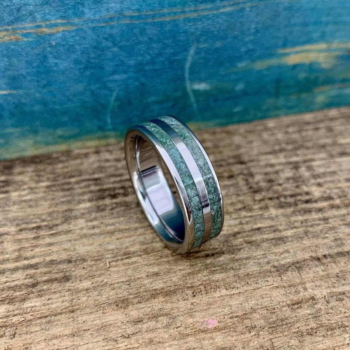 A titanium ring featuring two inlaid channels of green moss agate rests upright on a rustic wooden surface.