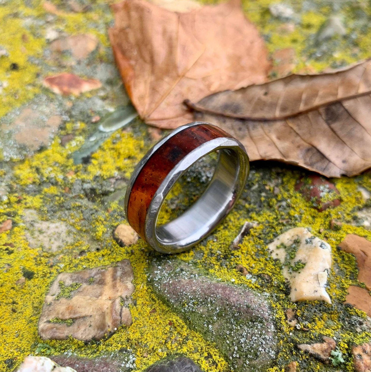 A wooden and metal ring placed upright on a textured, moss-covered stone near a dry leaf.