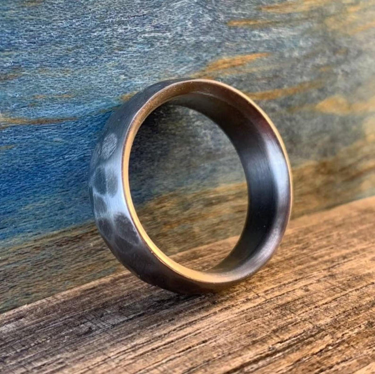 A silver-colored hammered metal ring standing upright, showing its textured outer surface and smooth inner band.