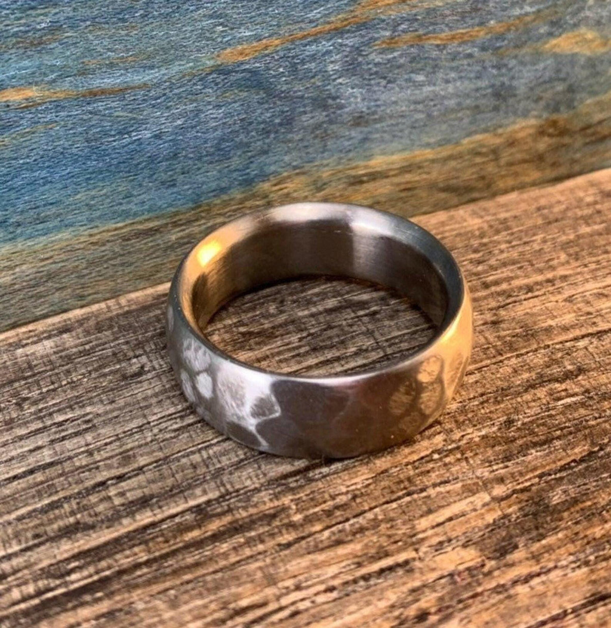 A silver-colored hammered ring lying flat on a wooden board with warm lighting on one side.