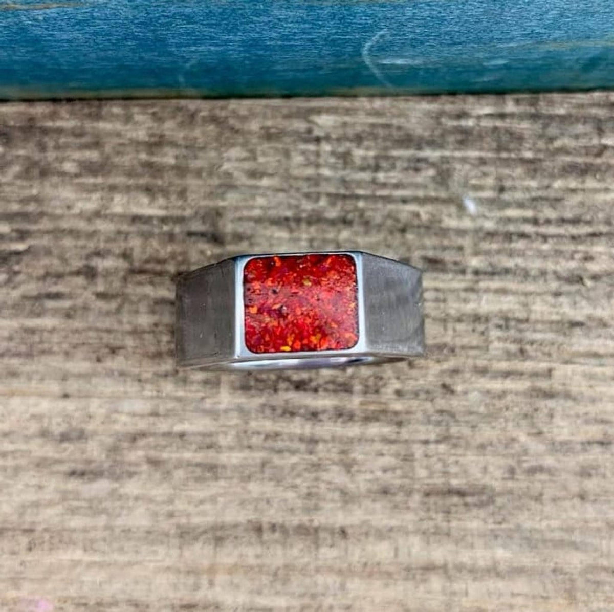 A top-down view of a silver signet ring featuring a mosaic red and orange opal inlay on a wooden surface.