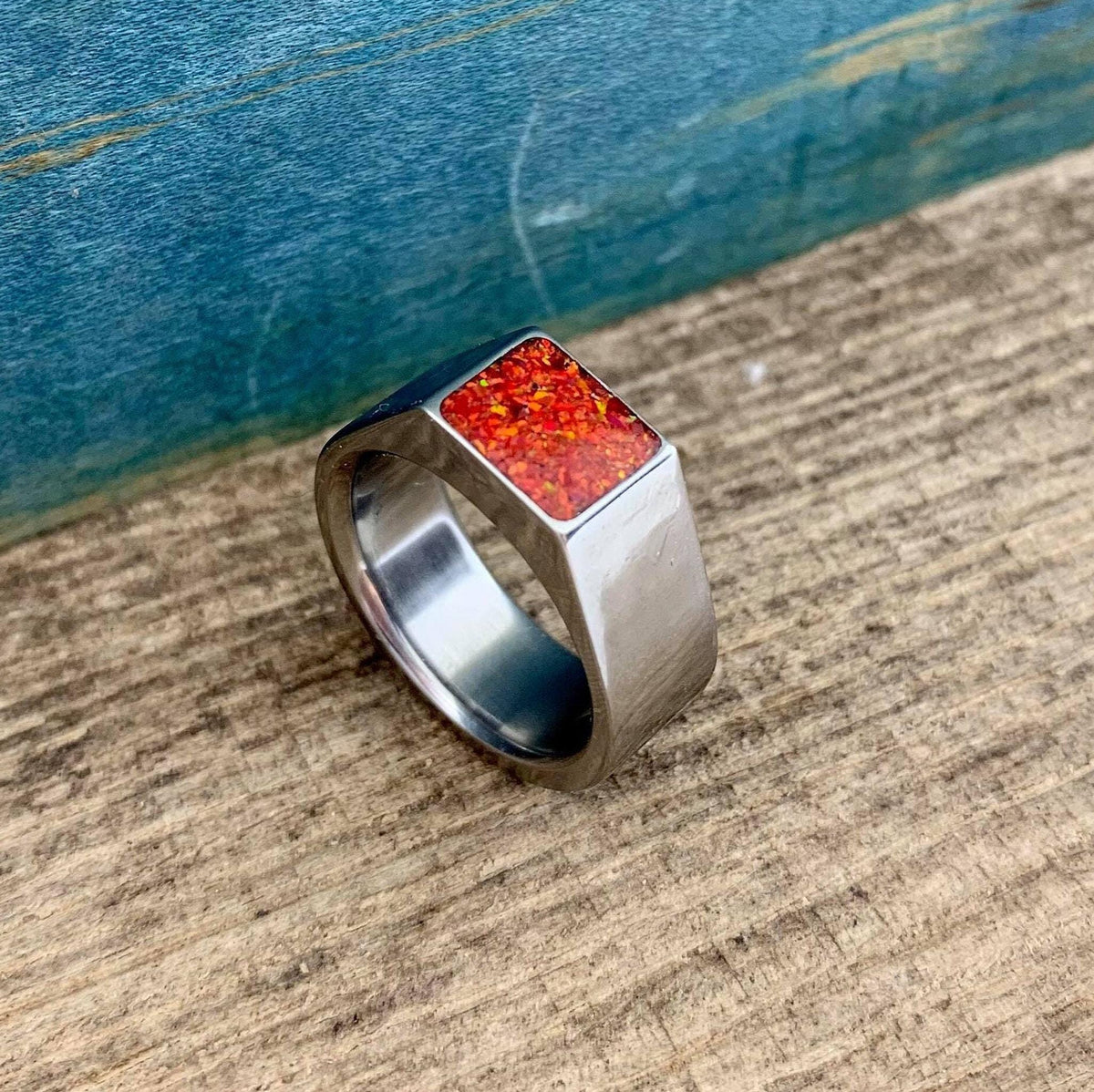 An angled view of a silver ring showcasing its geometric signet top filled with a red and orange speckled opal.