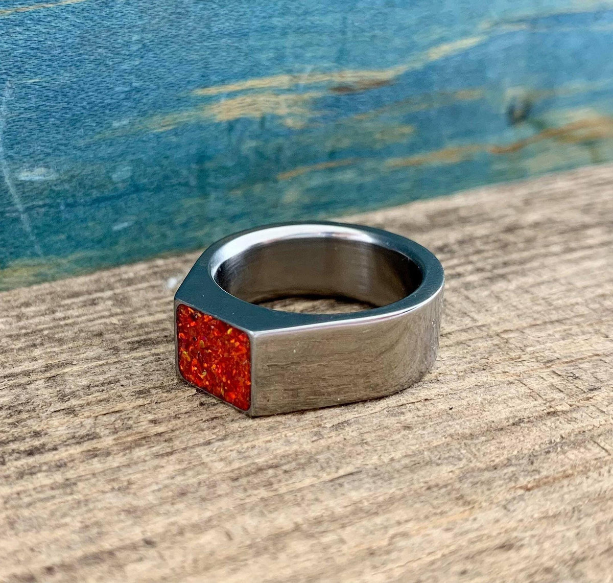 A silver signet ring with a red opal inlay is displayed on its side on a rustic wooden board.