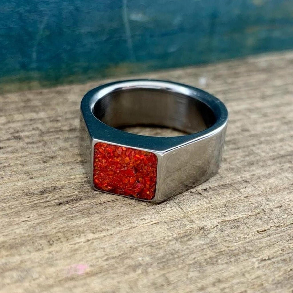 A close-up shot of a polished silver signet ring featuring a rectangular orange opal stone set on a wooden surface.