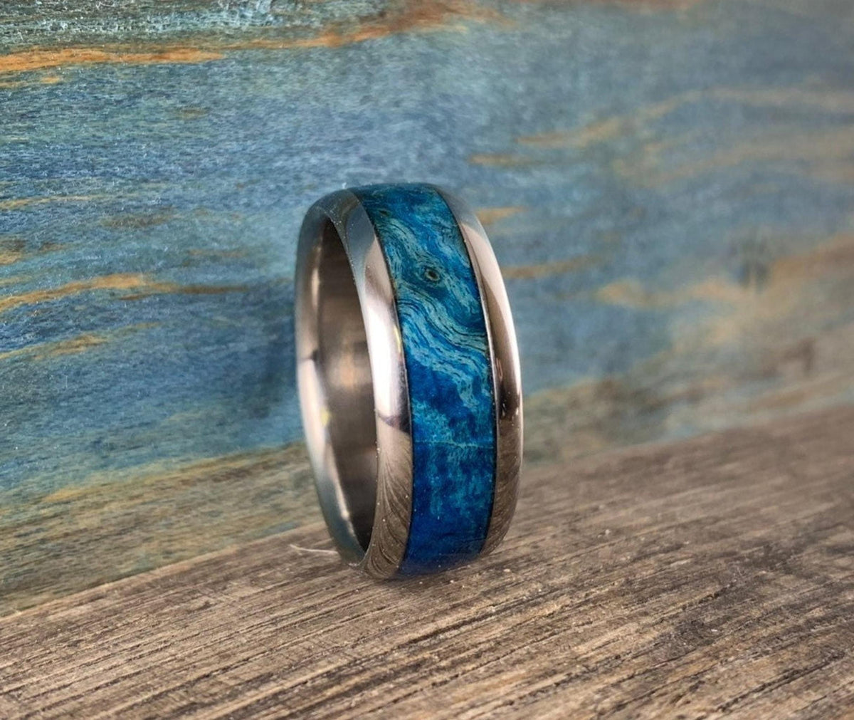 A three-quarter view of the blue wood inlay ring on a rustic wooden surface.